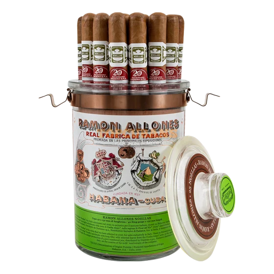 A clear cylindrical cigar storage jar with a copper-toned metal lid and wire handles, filled with brown cigars at the top. The front label reads Ramón Allonés and shows illustrated branding and the text '20 Aniversario'.